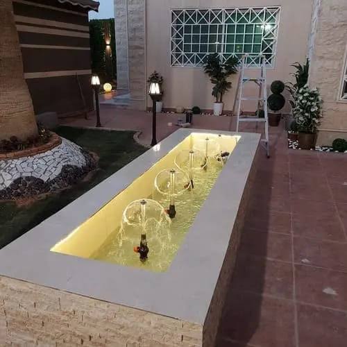 نافورة أرضية مخفية بفوهات مدمجة داخل حوض مضاء في فناء فيلا