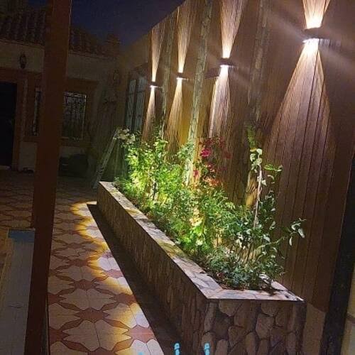 حوض زراعي حجري مرتفع مع نباتات وزهور وإضاءة جدارية ليلية